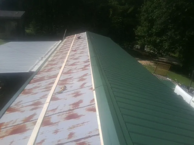 Old rusted panels beside newly installed green metal roofing — Wind Damage Roof Repair by Roofing Brothers in Adrian
